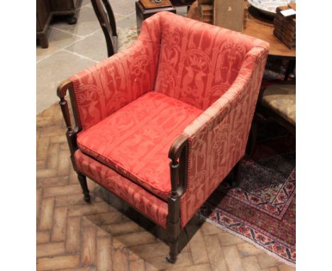 An Edwardian mahogany tub chair, covered in red classical pattern fabric, the padded arms extending to tapering pilasters inl