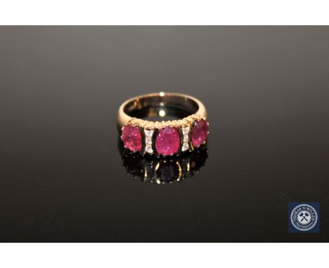 A 14ct yellow gold ruby and diamond ring, with three, central, reddish-pink rubies in claw settings weighing a total of 3.11 