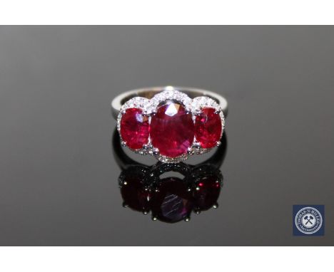 A 14ct white gold ruby and diamond ring, three oval-cut deep red rubies weighing a total of 5.44 carats within claw settings,