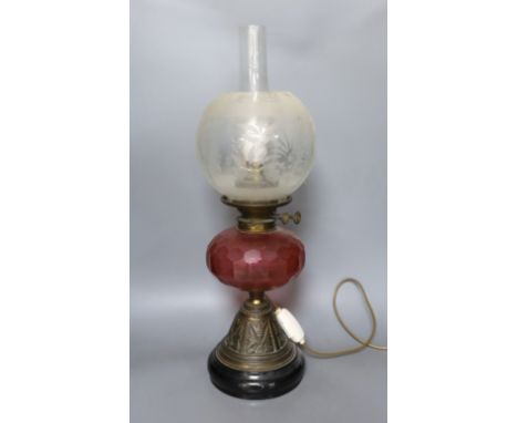 An Edwardian oil lamp with ruby glass font, later inverted to electricity,57 cms high including funnel.