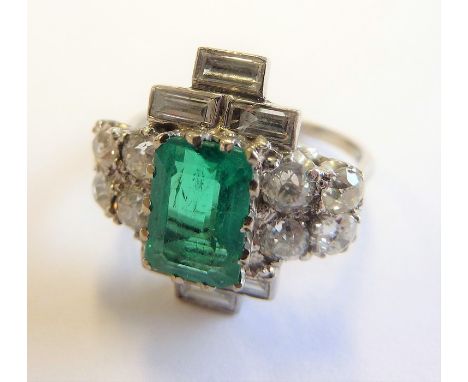 A platinum and diamond dress ring; vertically set with a vertical emerald surmounted with three baguette-cut diamonds and thr