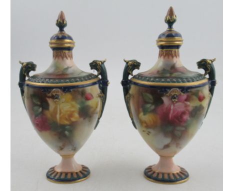 A pair of Royal Worcester Hadley ware covered vases, painted with roses, with griffin mask handles, both finials re-glued and