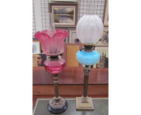 A Victorian oil lamp with a cranberry glass reservoir on a brass column and ebonised base together with another oil lamp with