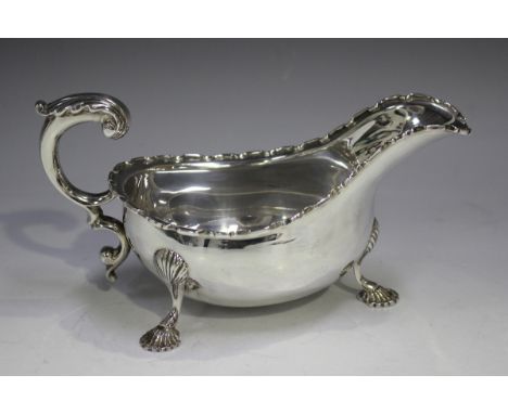 A George VI silver sauceboat with undulating rim and foliate capped flying scroll handle, raised on scallop shell shouldered 