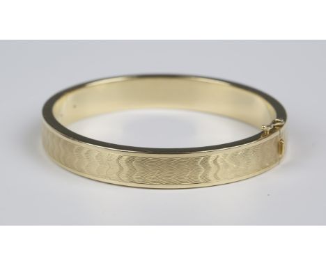 A gold oval hinged bangle with engine turned decoration, on a snap clasp, detailed '585', weight 34.5g, inside width 6.2cm.Bu