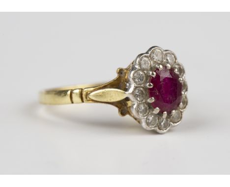 An 18ct gold, ruby and diamond oval cluster ring, claw set with the oval cut ruby within a surround of twelve circular cut di