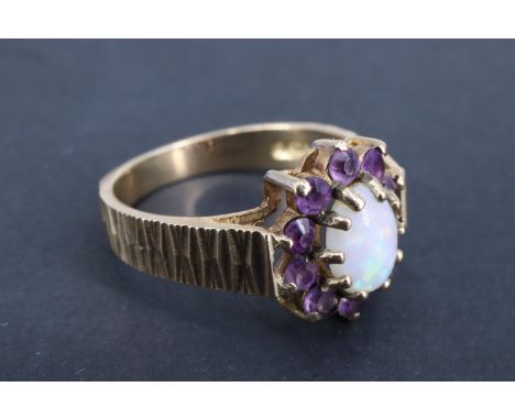 A 1970s opal and amethyst ring, the central 7 x 5 mm oval cabochon set above 10 surrounding 2 mm amethysts, set between squar