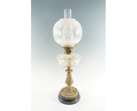 An early 20th Century brass and glass oil lamp, the cast base bearing masks and musical instruments, having a glass font and 