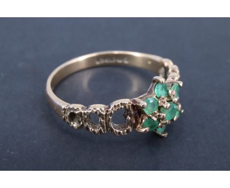 A 1970s daisy set emerald ring, the central 2 mm brilliant set above six surrounding similar stones, between textured shoulde