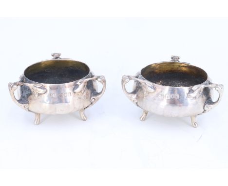 A pair of Art Nouveau silver salt cellars, of oblate planished form with gilt interiors, each having three feet rising to nat
