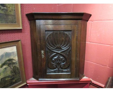 An early 19th Century oak hanging corner cupboard, the single door with carved sea creatures below a clam shell (with key), 7