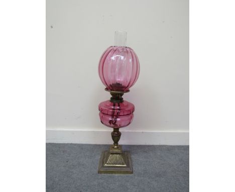 A Victorian oil lamp, fluted faceted base, cranberry reservoir and shade on brass base