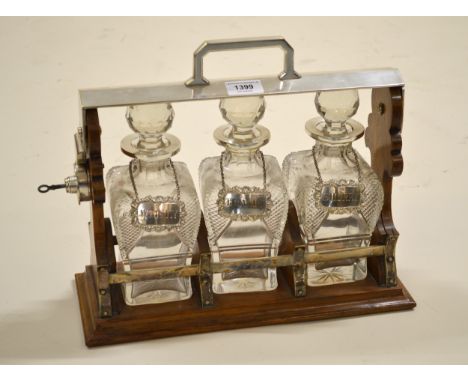 Early 20th Century oak and silver plate mounted three bottle tantalus with original shaped hobnail cut decanters, with a set 