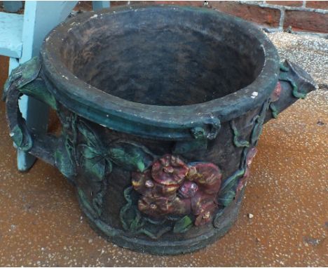 A large concrete garden planter in the form of a watering can decorated with flowers