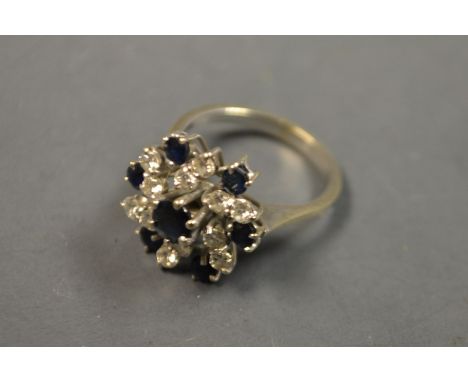A diamond and sapphire cluster ring, stepped spiralling floral crest, set with six pairs of round brilliant cut diamonds, and
