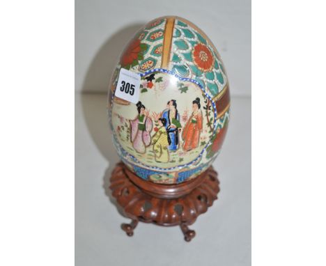 A modern Oriental ceramic egg-shaped ornament decorated typical garden scenes and floral panels, on carved wooden circular st