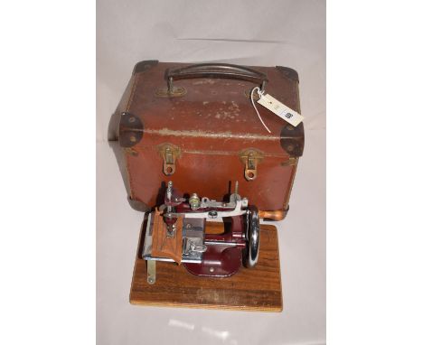 A miniature first half 20th Century hand-cranked sewing machine, in maroon and chromed metal finish on wooden plinth base; to
