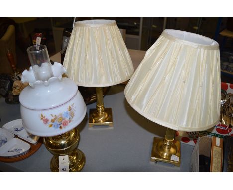 Two brass table lamps; and a brass oil lamp with florally decorated shade.