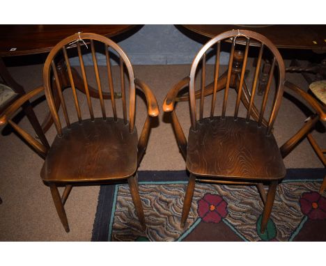 A pair of Ercol style stained elm elbow chairs, the solid shaped elm seats raised on turned legs joined by stretchers, stampe