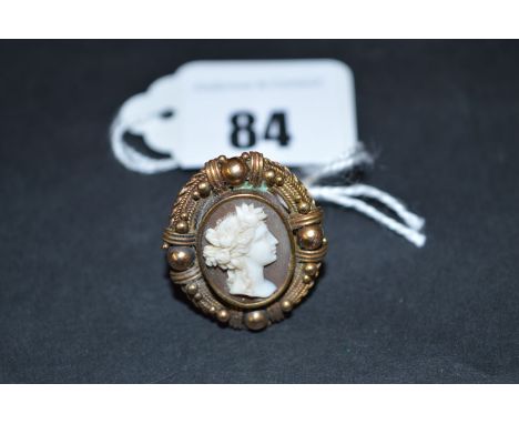 A carved shell cameo ring depicting a female bust with flowers in her hair, surrounded by yellow metal beadwork mount, on sha