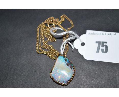 A black opal pendant, the rough opal in claw mount, on yellow metal link chain.