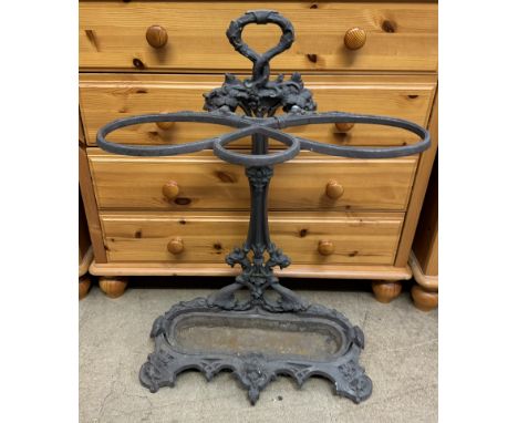 A cast iron stick stand with a leaf cast handle and three strap rests, the oval base with cast feet