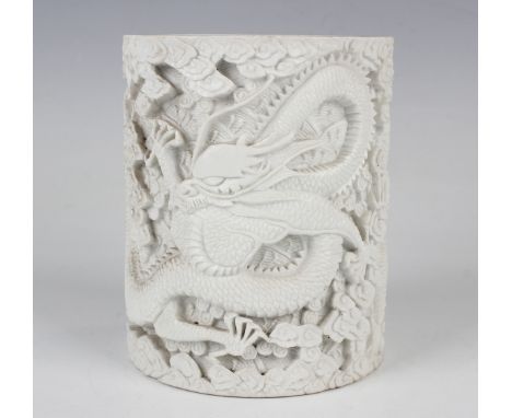 A Chinese white biscuit porcelain brushpot of cylindrical form, the exterior carved in relief with two dragons amidst clouds,