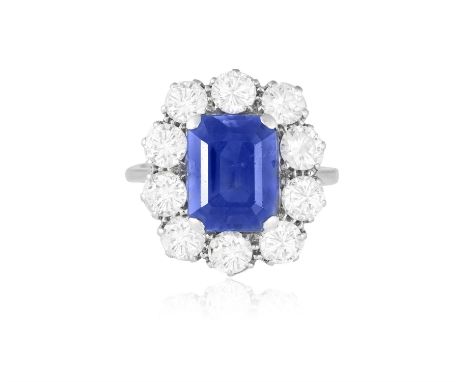 A SAPPHIRE AND DIAMOND CLUSTER RINGThe cut-cornered rectangular sapphire weighing approximately 4.50cts within a four-claw se
