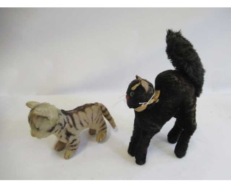 Two Steiff cats, comprising a tabby with green glass eyes and a 1950s Schwarzer Kater with silver button and partial label (E