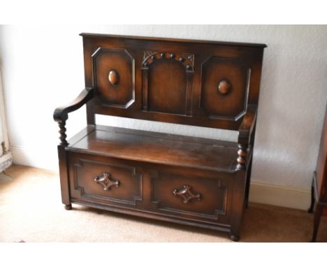 A 1920s oak settle, with panelled back and box seat, on turned feet, height 113cm, width 121cm, depth 48cm.PROVENANCE: The Ra