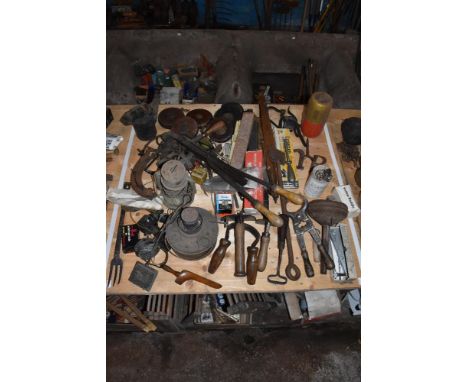 A collection of vintage agricultural tools and metal items, including carpentry tools, a branding iron, vintage measuring tap