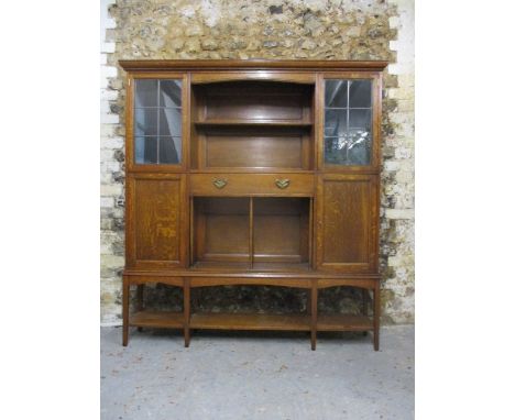 An Arts & Crafts oak display cabinet attributed to Liberty having a moulded cornice over two shelves, a drawer and another sh