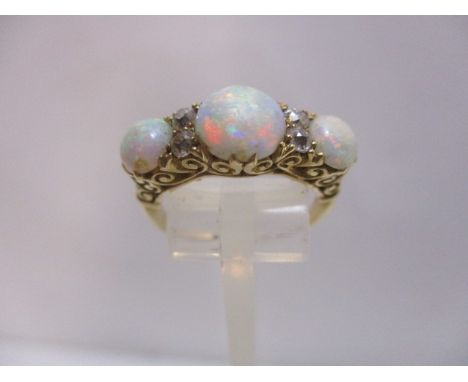 A gold coloured metal ring with three opals and four diamonds, in scrolled, claw settings