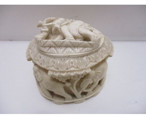 An early 20th century carved ivory pot and cover, the lid decorated with an elephant carrying a branch, the body with a ring 