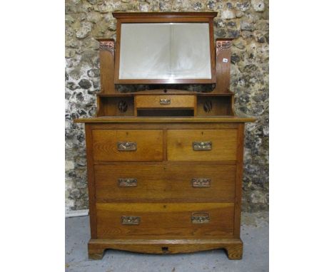 An Arts & Crafts oak dressing table, the mirror pivoting on rectangular horns with copper panels, embossed with styalized flo