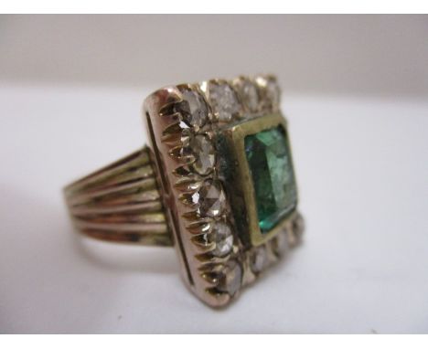 A 19th century yellow metal ring set with an emerald cut emerald within fourteen old cut diamonds