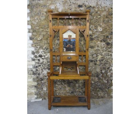 An Arts & Crafts oak hallstand having a shelf over a mirror, flanked by anodized hooks, fretwork bracket and pillars, above a