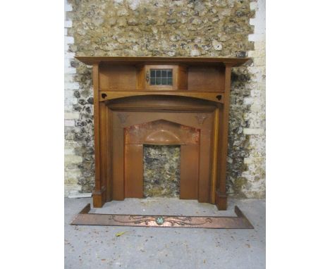 An Arts & Crafts oak fire surround having a shelf over a lead glazed door with canted flanks above a frieze, with heart motif