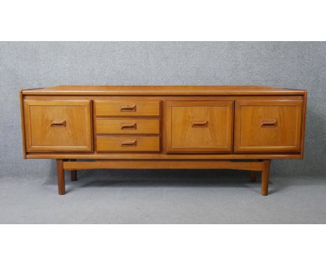 A mid century vintage teak sideboard with drawers flanked by cupboards on stretchered shaped supports. H.78 W.198 W.44cm 