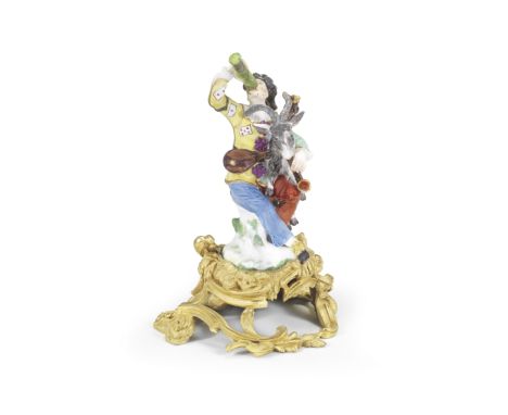 A rare Meissen ormolu-mounted figure of Harlequin with a 'Pass Glass', circa 1740Modelled by J.J. Kaendler, seated on a rocky