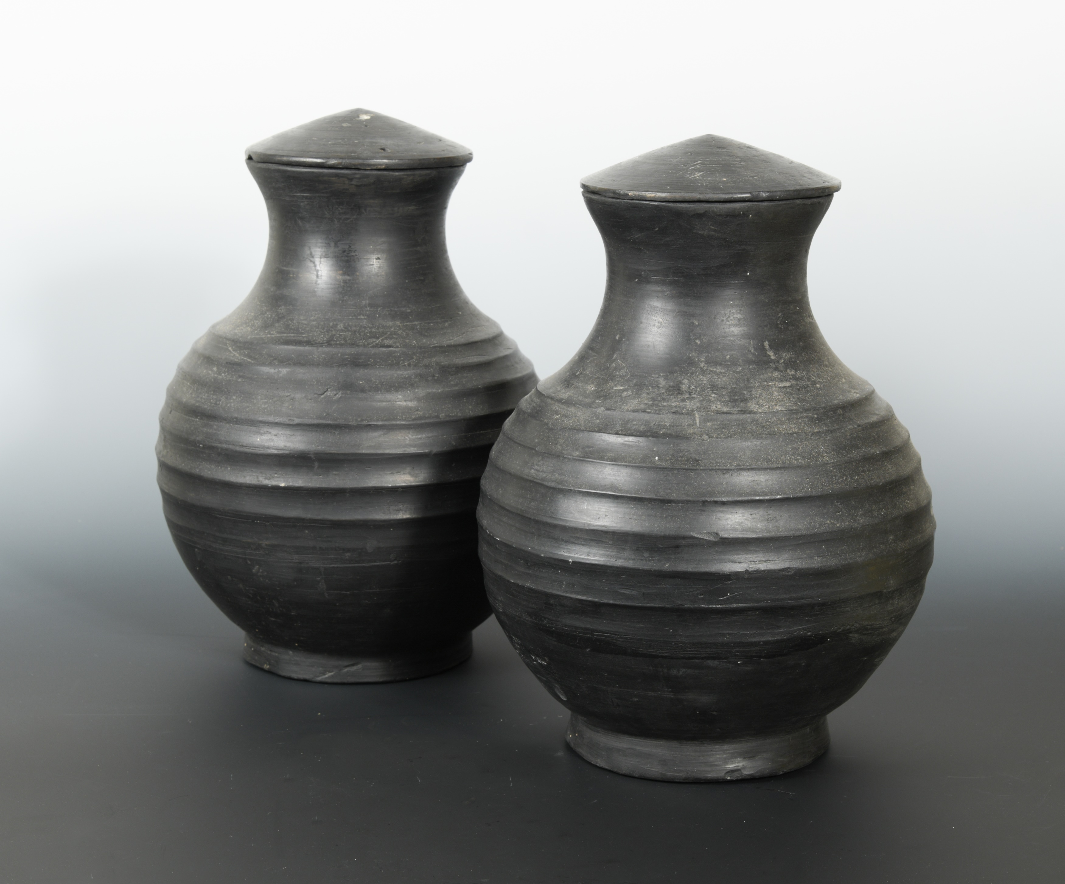 A pair of Chinese burnished pottery lidded vases, with deeply ribbed