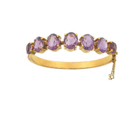 An Amethyst Bangle seven graduated oval cut amethysts in yellow claw settings, to a plain polished hinged backinner measureme