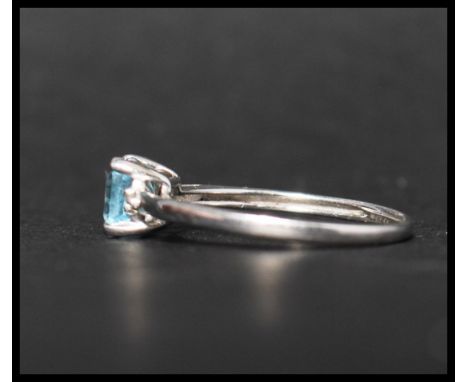 A hallmarked 9ct white gold ring set with a cushion cut pale blue stone flanked by two round cut diamonds. Hallmarked London.