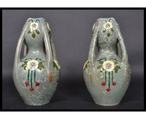 A pair of early 20th century Art Nouveau ceramic four handled vases having painted floral sprays and medallions. The bulbous 