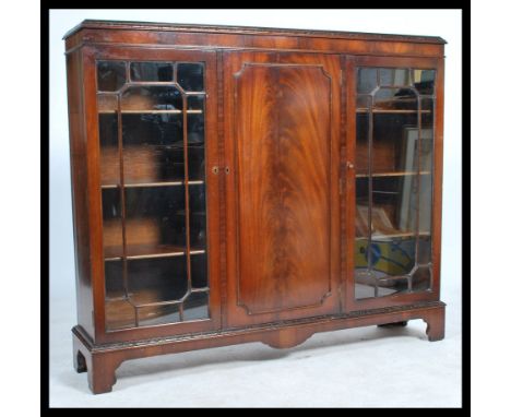 An early 20th century mahogany display cabinet bookcase, central panel cupboard door flanked by astral glazed doors raised on