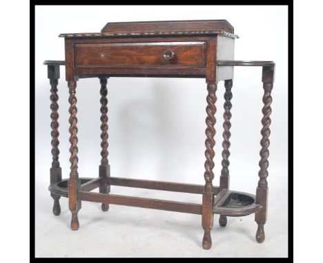 A 1920's oak barley twist stick stand having hooped stick rests either side of a singel drawer being raised on barleytwist co