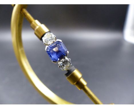 AN 18ct STAMPED CEYLON BLUE SAPPHIRE AND DIAMOND RING. THE CENTRAL SAPPHIRE IS A CORNER CLAW SET SQUARE RADIANT CUT FLANKED B