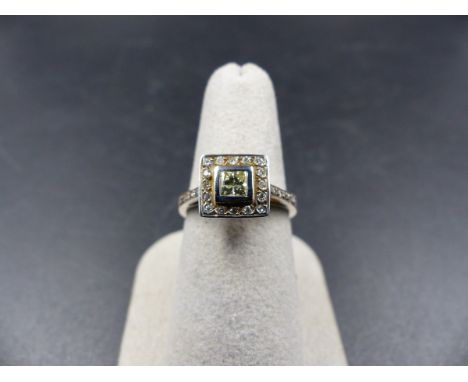 A 14K STAMPED WHITE METAL DIAMOND RING. THE CENTRAL DIAMOND IS PRINCESS CUT IN A RUB OVER SETTING SURROUNDED BY A HALO OF DIA