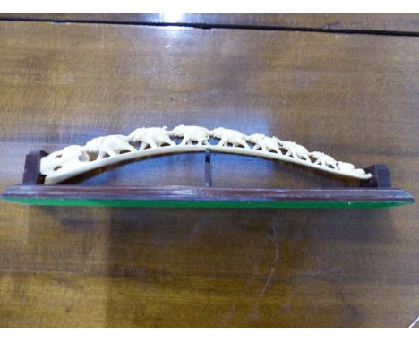 A TUSK PIERCED AND CARVED WITH SEVEN ELEPHANTS TRUNK TO TAIL WALKING ACROSS THE ARCHED PATH, ON  MAHOGANY STAND.   53cms.