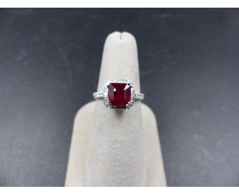 A WHITE METAL RUBY AN DIAMOND RING, STAMPED 750. THE CENTRAL RUBY IS SUSPENDED IN A DOUBLE FOUR CLAW SETTING SURROUNDED BY A 